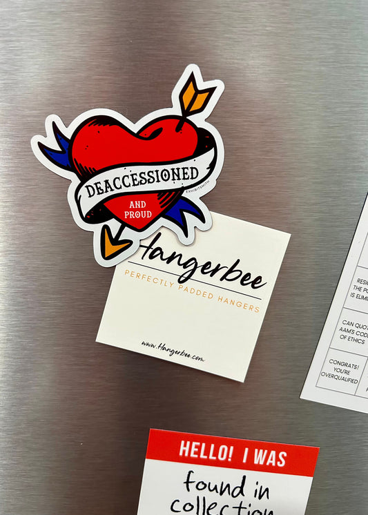 Hangerbee padded clothing hangers has developed magnets, stickers, keychains, pins, and more, with museum collections professionals in mind. This image shows a Deaccessioned and Proud magnet and a Found in Collection magnet holding up a square Hangerbee business card on a refrigerator.