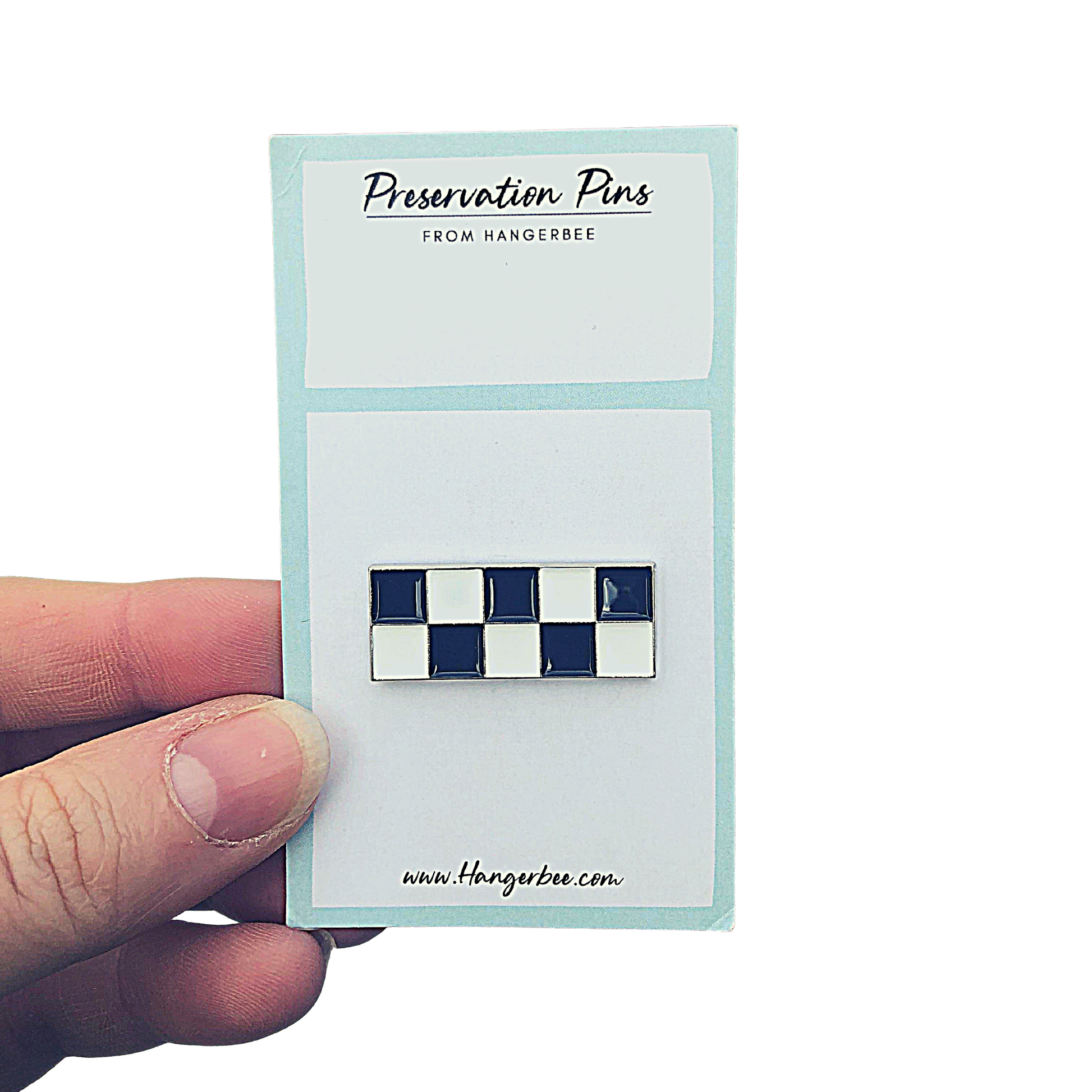 Photo of Hangerbee padded hanger's Collections Toolbox Lapel Pin of a black and white checkered photography scale (1/4") on a card that's designed to look like an acid-free box lined with ethafoam. The card is on a small, cotton bag which is on a wood table.