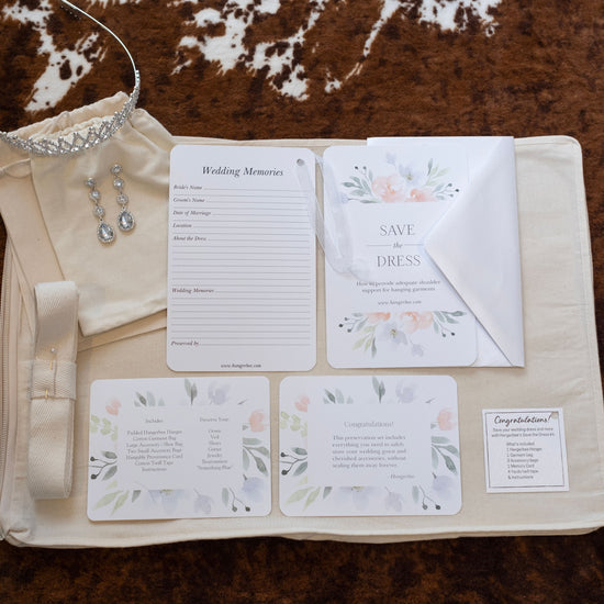 image featuring items in hangerbee padded hanger's save the dress, wedding dress preservation kit. The kit includes an heirloom safe, preservation quality padded clothes hanger, a large cotton garment bag, a large, zippered, cotton accessory bag and two small cotton drawstring bags, yards of cotton twill take, a wedding memories memory card, and instructions.