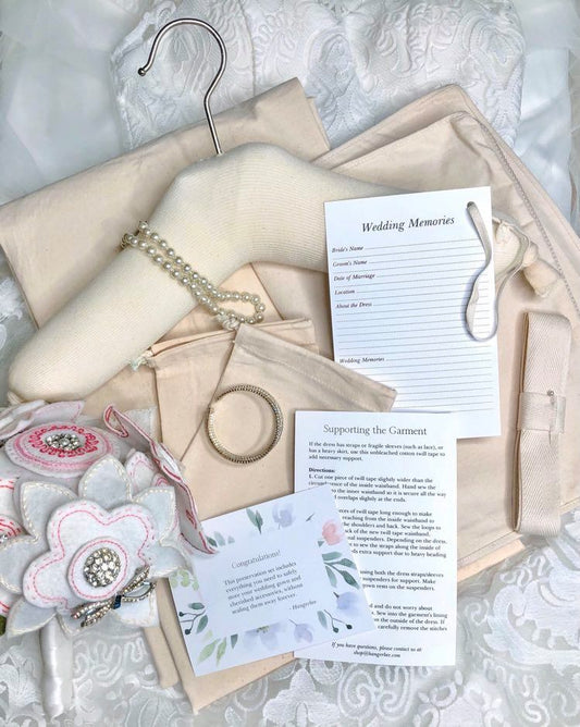image featuring items in hangerbee padded hanger's save the dress, wedding dress preservation kit. The kit includes an heirloom safe, preservation quality padded clothes hanger, a large cotton garment bag, a large, zippered, cotton accessory bag and two small cotton drawstring bags, yards of cotton twill take, a wedding memories memory card, and instructions.
