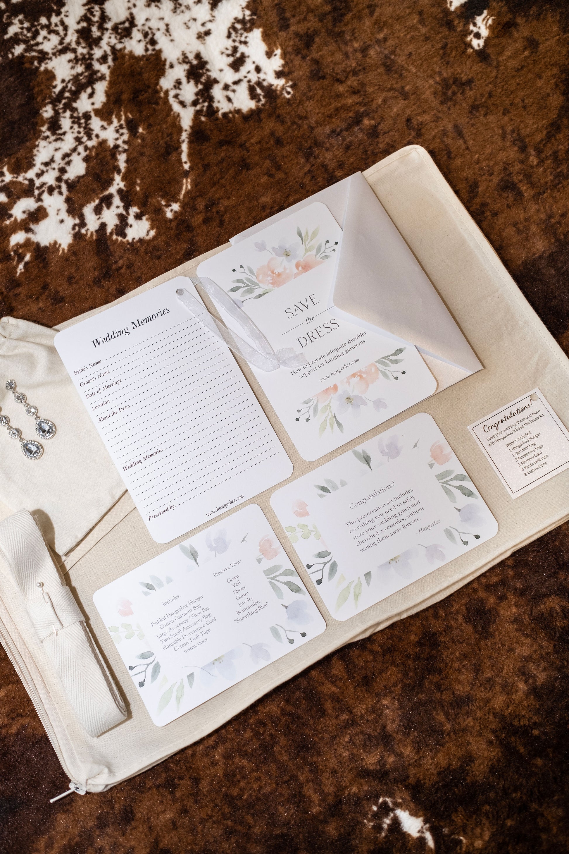 image featuring items in hangerbee padded hanger's save the dress, wedding dress preservation kit. The kit includes an heirloom safe, preservation quality padded clothes hanger, a large cotton garment bag, a large, zippered, cotton accessory bag and two small cotton drawstring bags, yards of cotton twill take, a wedding memories memory card, and instructions.